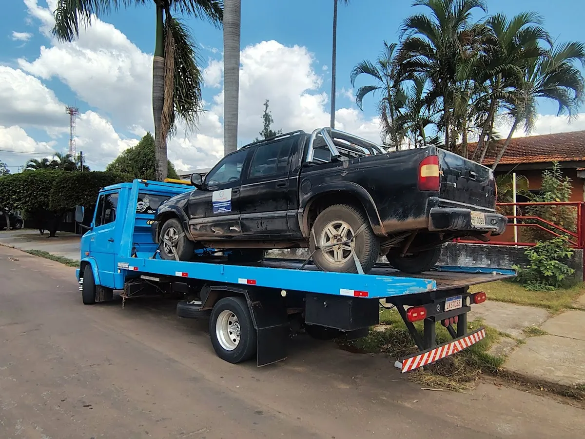 Caminhão guincho azul transportando uma picape preta na plataforma